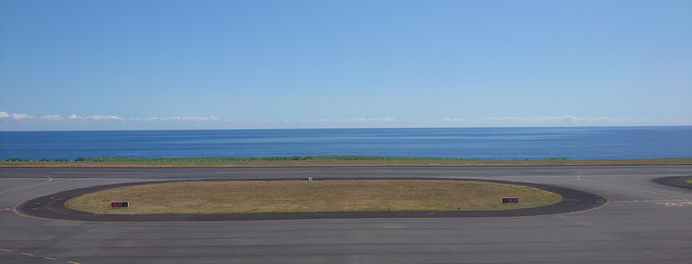 Blick auf Flugzeug-Landebahn mit Meer im Hintergrund 